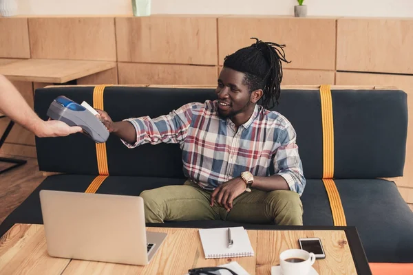 Client afro-américain payant avec carte de crédit et terminal dans le café — Photo de stock