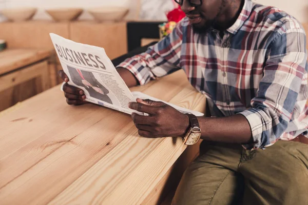 Vista cortada do homem americano africano sentado no balcão de bar e lendo jornal de negócios — Fotografia de Stock