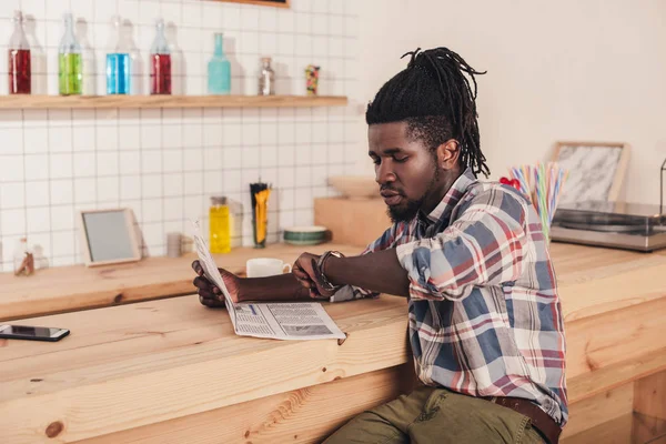 African american man sitting at bar counter and reading business newspaper — Stock Photo