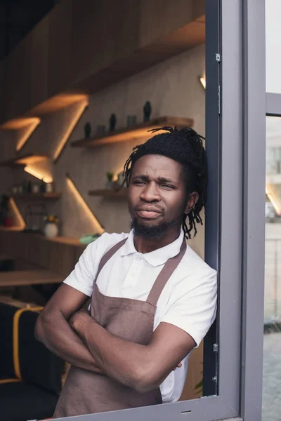 African american cafe owner in apron standing with crossed arms at entrance — Stock Photo