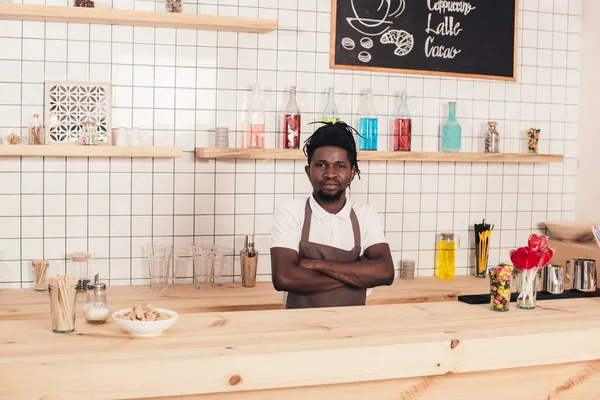 African american bartender with crossed arms standing at bar counter — Stock Photo