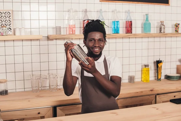 Barman afroamericano haciendo cóctel en coctelera en el mostrador del bar - foto de stock