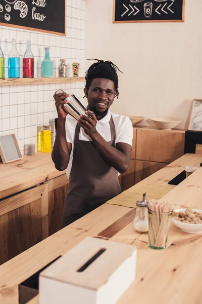 Barman afroamericano haciendo cóctel en coctelera en el mostrador del bar - foto de stock
