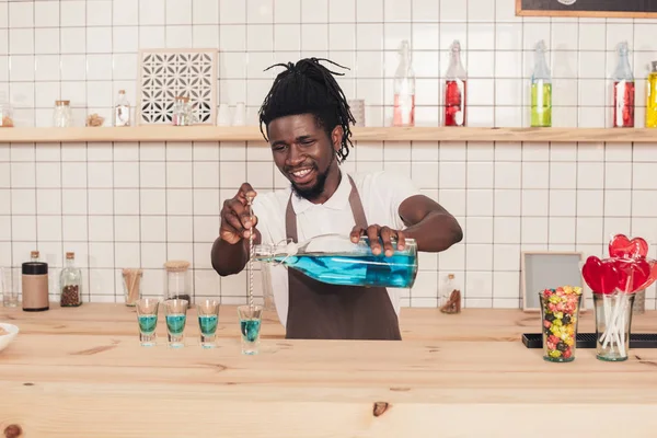 African american bartender pouring blue drink into shot glasses at bar counter — Stock Photo