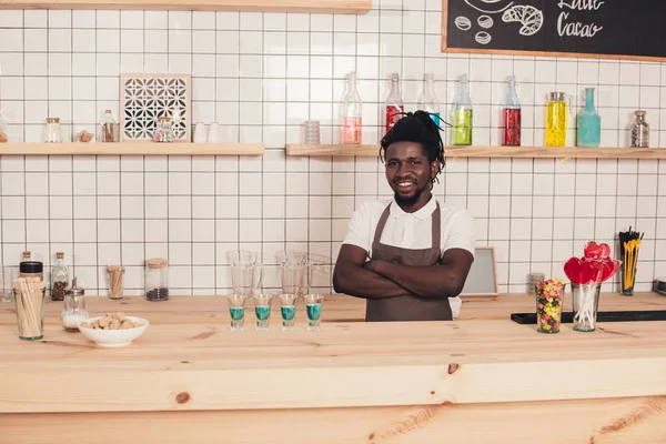 Sorridente barman americano africano com coquetéis azuis em copos de tiro no balcão de bar — Fotografia de Stock