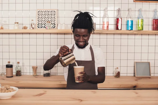 Barista afroamericano haciendo café en taza desechable en el mostrador de bar - foto de stock