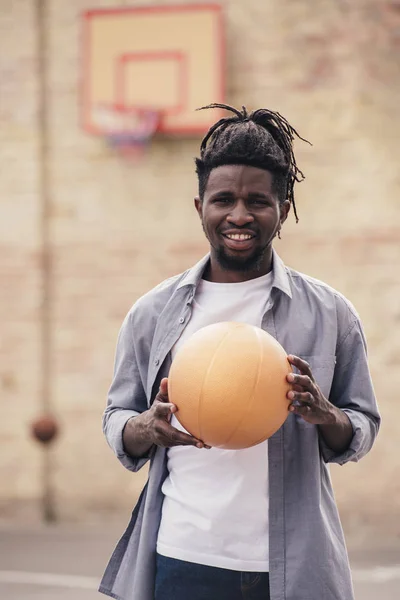Lächelnder afrikanisch-amerikanischer Mann hält Basketballball auf der Straße — Stockfoto