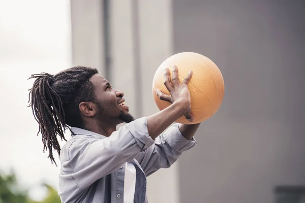 Hombre afroamericano lanzando pelota de baloncesto en la calle - foto de stock