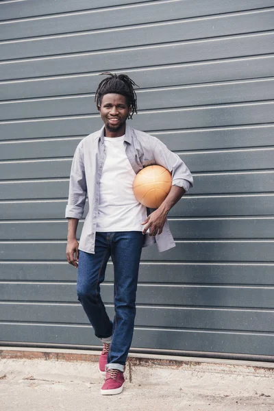 Guapo sonriente afroamericano hombre con pelota de baloncesto en la calle - foto de stock