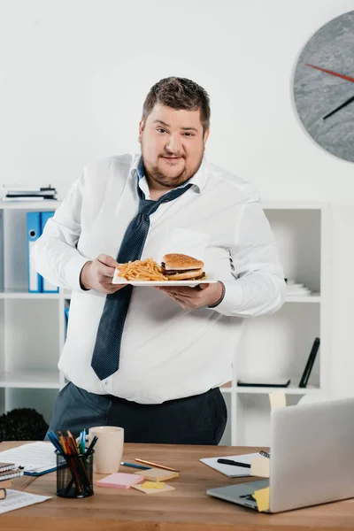 Homem de negócios com excesso de peso com junk food no escritório — Fotografia de Stock