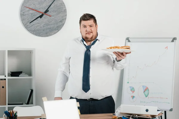 Gordo hombre de negocios con comida chatarra en la oficina - foto de stock