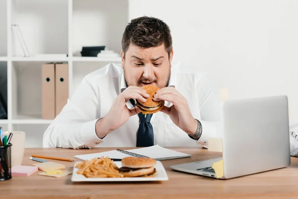 Hombre de negocios con sobrepeso comiendo comida basura en la oficina - foto de stock