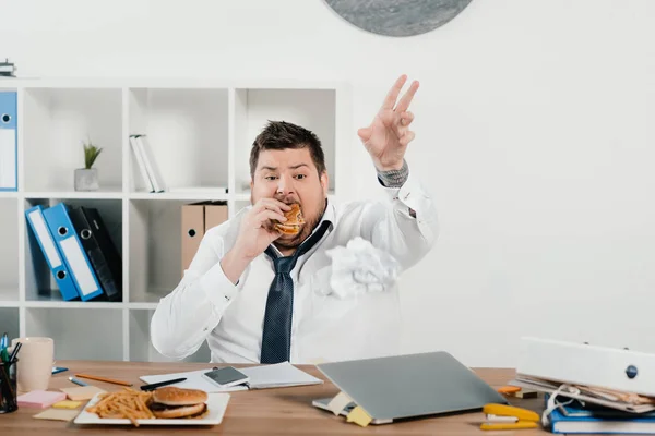 Hombre de negocios con sobrepeso comiendo hamburguesas y papas fritas en la oficina - foto de stock