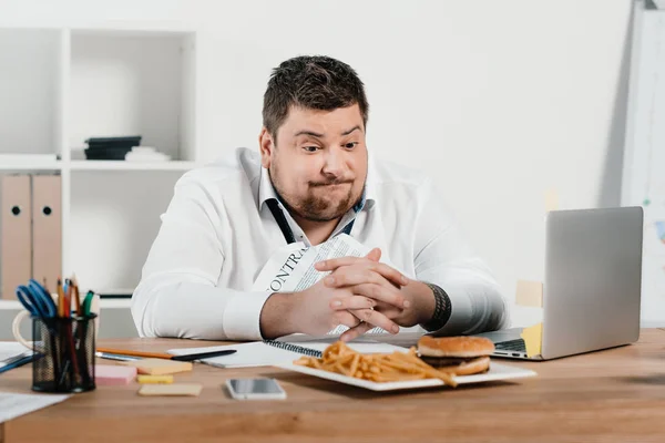 Hombre de negocios con sobrepeso almorzando con hamburguesa y papas fritas en la oficina - foto de stock