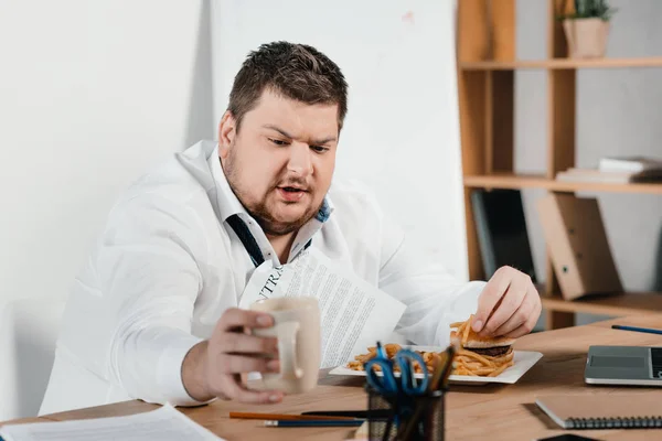 Homem de negócios com sobrepeso comer fast food e beber café no escritório — Fotografia de Stock