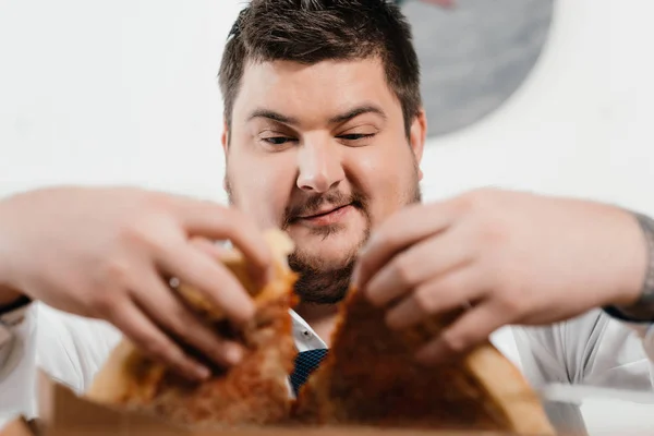 Foco seletivo do empresário com excesso de peso comendo pizza no almoço no local de trabalho — Fotografia de Stock