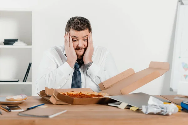 Sobrepeso sorprendido empresario con pizza en el lugar de trabajo - foto de stock