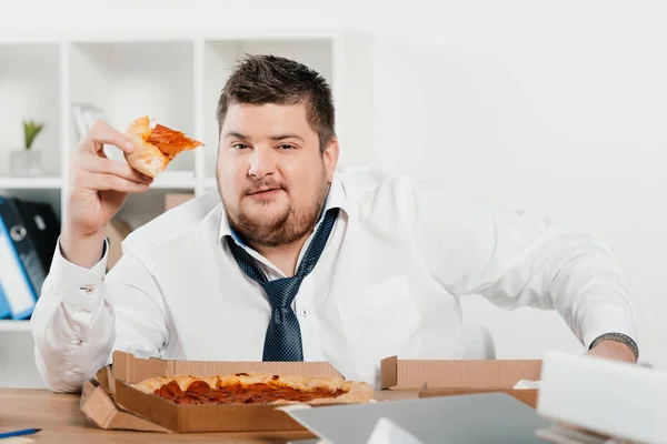 Übergewichtiger Geschäftsmann isst Pizza am Arbeitsplatz — Stockfoto