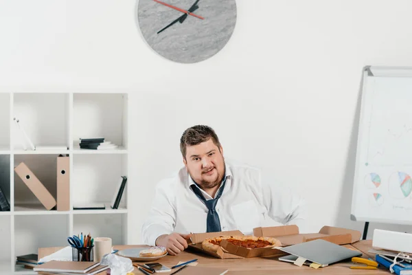 Übergewichtiger Geschäftsmann isst Pizza am Arbeitsplatz im Büro — Stockfoto