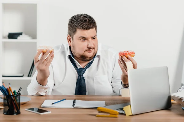 Hombre de negocios con sobrepeso comiendo donas en el lugar de trabajo - foto de stock