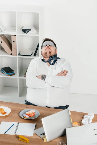 Hombre de negocios gordo en la máscara de dormir relajarse en el lugar de trabajo - foto de stock