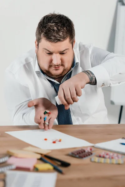 Fat businessman with pills sitting at workplace in office — Stock Photo