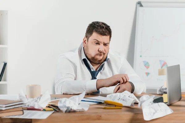 Confused overweight businessman sitting at workplace with crumpled papers — Stock Photo