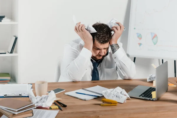 Tired overweight businessman sitting at workplace with crumpled papers — Stock Photo