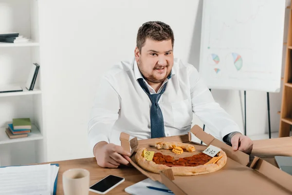 Hombre de negocios con sobrepeso comiendo pizza en el lugar de trabajo en la oficina - foto de stock