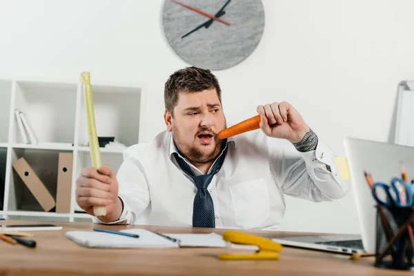 Hombre de negocios con sobrepeso comiendo verduras frescas en el lugar de trabajo en la oficina - foto de stock