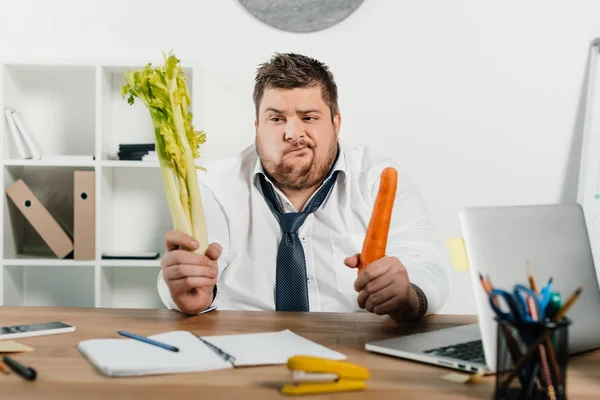 Confundido hombre de negocios con sobrepeso mirando verduras frescas - foto de stock