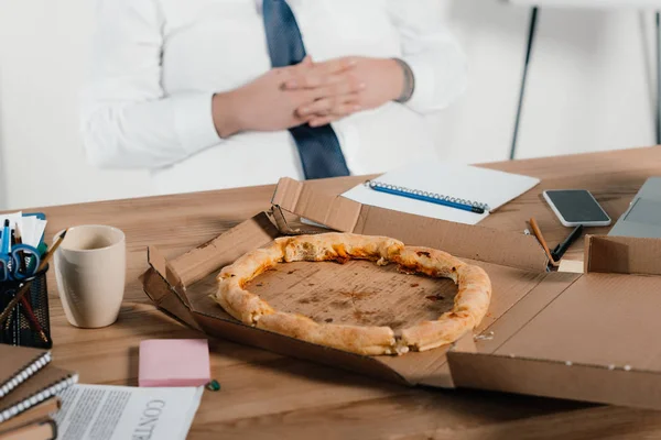 Cropped view of fat businessman eating pizza at workplace — Stock Photo