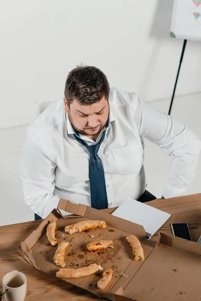Vista aérea del hombre de negocios con sobrepeso comiendo pizza en el lugar de trabajo en la oficina - foto de stock