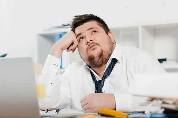 Thoughtful fat businessman with laptop at workplace in office — Stock Photo