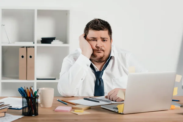 Aburrido hombre de negocios con sobrepeso trabajando con bloc de notas y portátil en la oficina - foto de stock