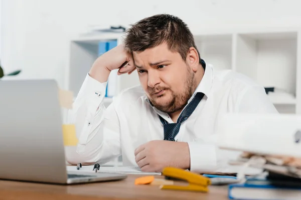 Confused overweight businessman working with laptop in office — Stock Photo