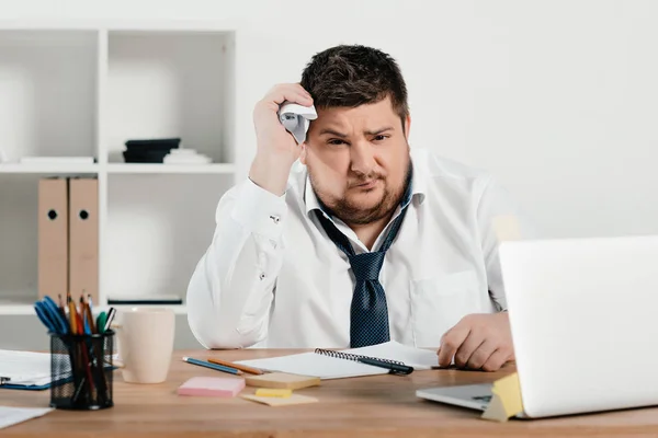 Hombre de negocios con sobrepeso que trabaja con bloc de notas y computadora portátil en la oficina - foto de stock