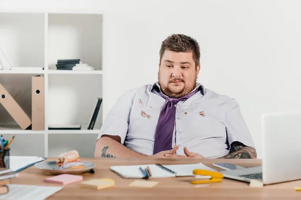 Надмірна вага бізнесмен дивиться на пончики, сидячи в офісі — стокове фото
