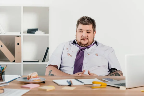 Homme d'affaires en surpoids regardant beignets tout en étant assis au bureau — Photo de stock