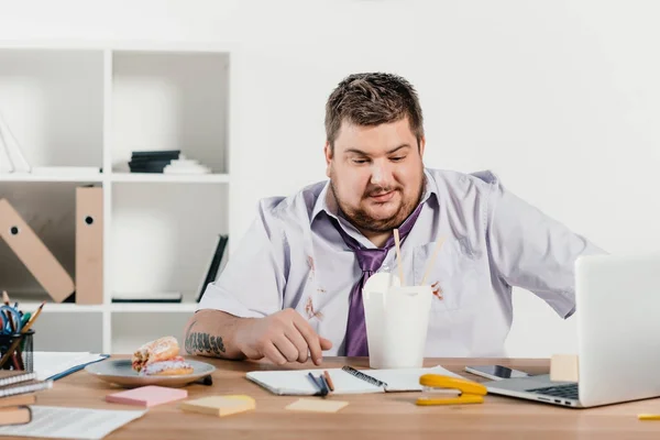 Hombre de negocios con sobrepeso comiendo fideos en el trabajo en la oficina - foto de stock