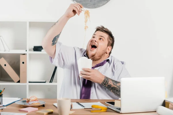 Aufgeregter übergewichtiger Geschäftsmann isst Nudeln am Arbeitsplatz im Büro — Stockfoto