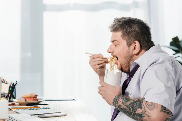 Übergewichtiger Geschäftsmann isst Nudeln am Arbeitsplatz im Büro — Stockfoto