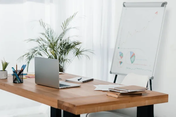 Lugar de trabajo con ordenador portátil y suministros de oficina en la oficina con pizarra blanca - foto de stock