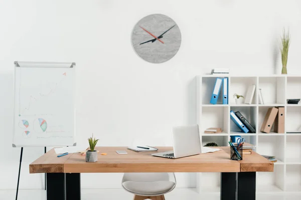Lieu de travail avec ordinateur portable et fournitures de bureau dans le bureau avec tableau blanc et horloge — Photo de stock