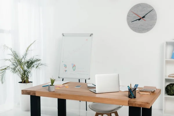 Lieu de travail avec ordinateur portable et fournitures de bureau dans le bureau avec tableau blanc et horloge — Photo de stock