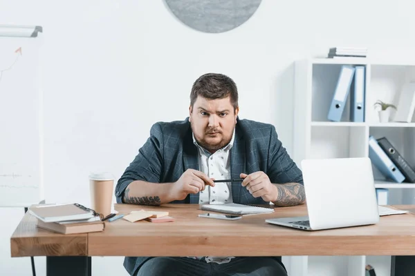 Hombre de negocios con sobrepeso sentado en el lugar de trabajo con computadora portátil y café - foto de stock