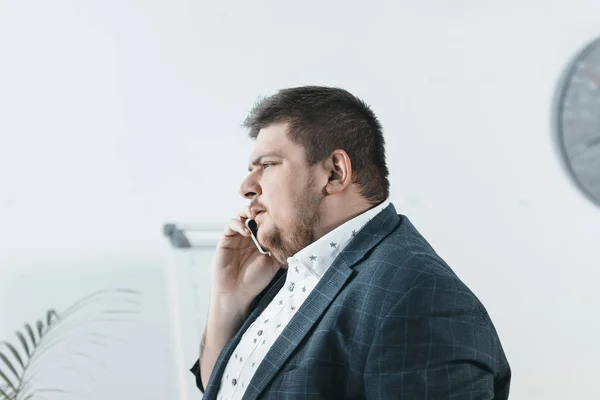 Толстый бизнесмен разговаривает на смартфоне в офисе — стоковое фото