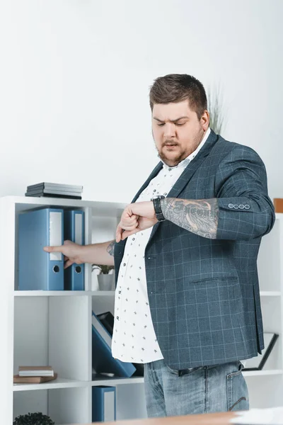 Overweight businessman looking at watch while taking folders with documents — Stock Photo