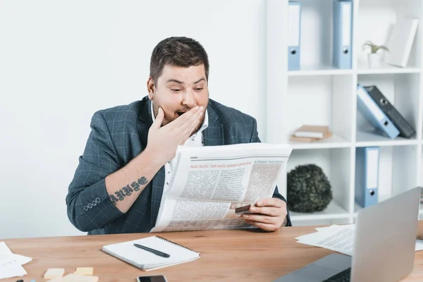 Hombre de negocios con sobrepeso en traje leyendo periódico en el lugar de trabajo - foto de stock