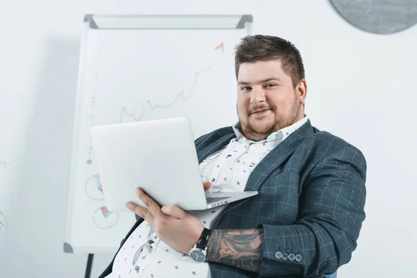 Бизнесмен с избыточным весом в костюме работает с ноутбуком в офисе — стоковое фото
